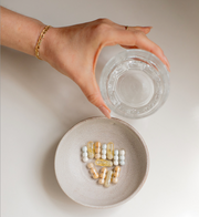 A hand holding a glass of water above a plate of vitamins, reflecting WeNatal's focus on prenatal supplements and wellness.